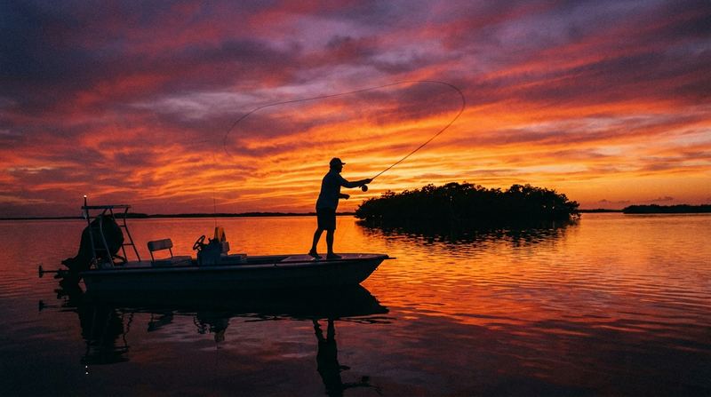 A fly angler casting off a skiff at a fiery Sarasota sunset over the flats