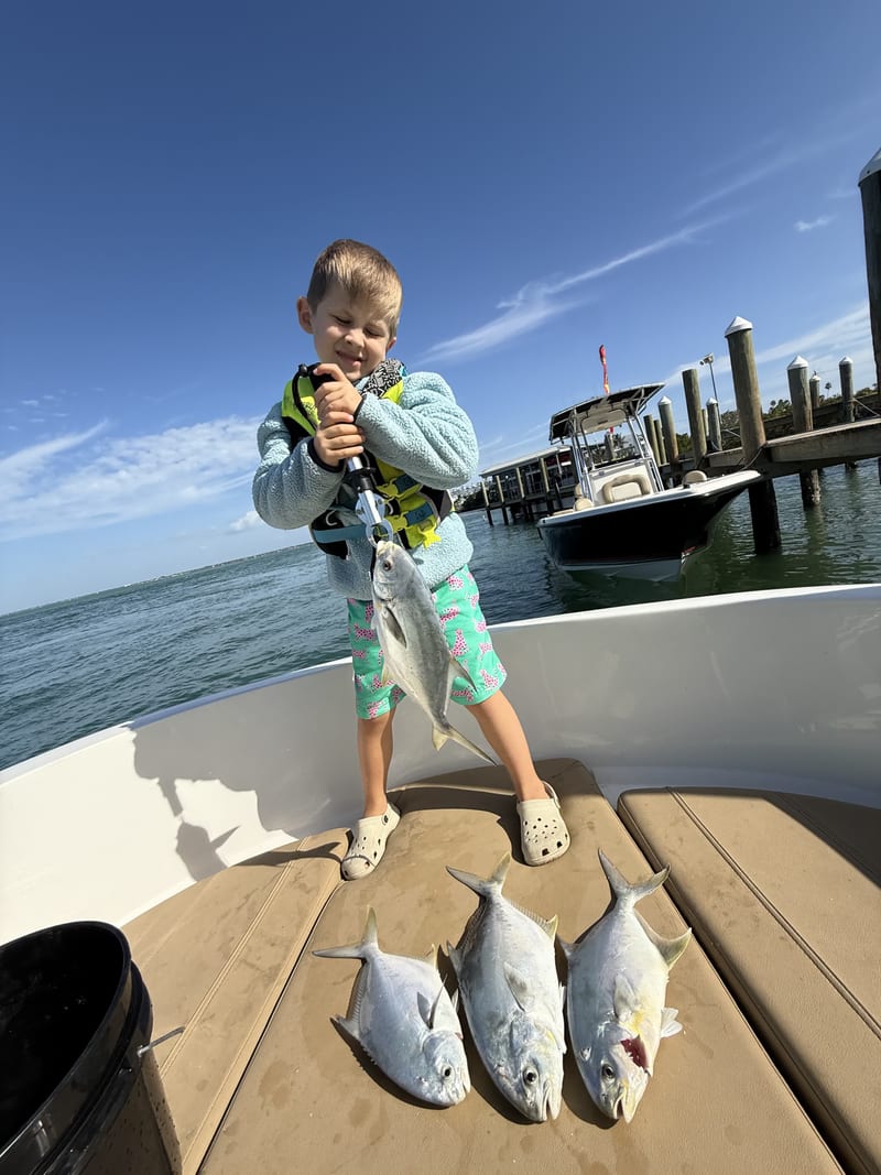 Young angler on a boat with a morning's catch of small jacks laid out on the deck