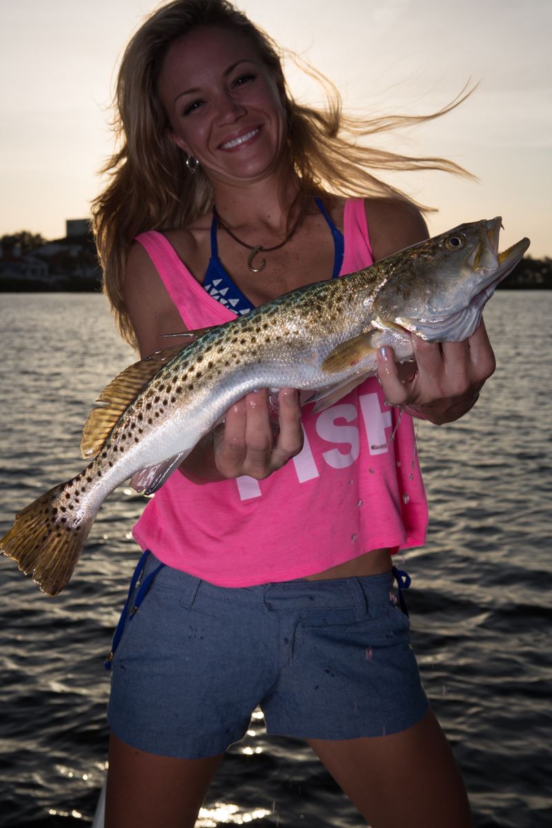 An angler on the water holding a heavy spotted seatrout, black spots along the flank