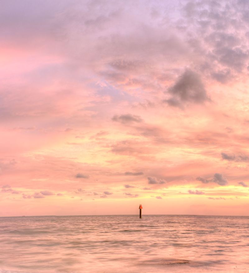 Pastel pink Gulf sky over calm nearshore water and a channel marker off Sarasota