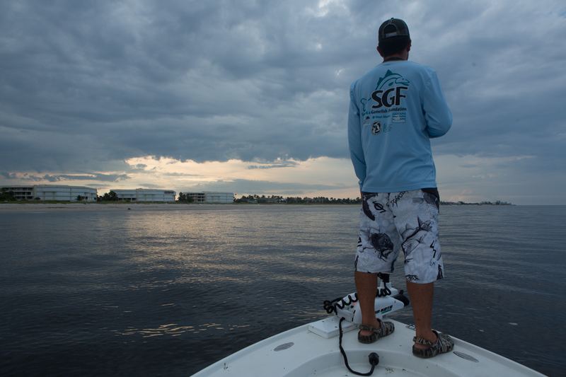 An angler on the bow of a skiff watching a dark front build over the pass at dusk