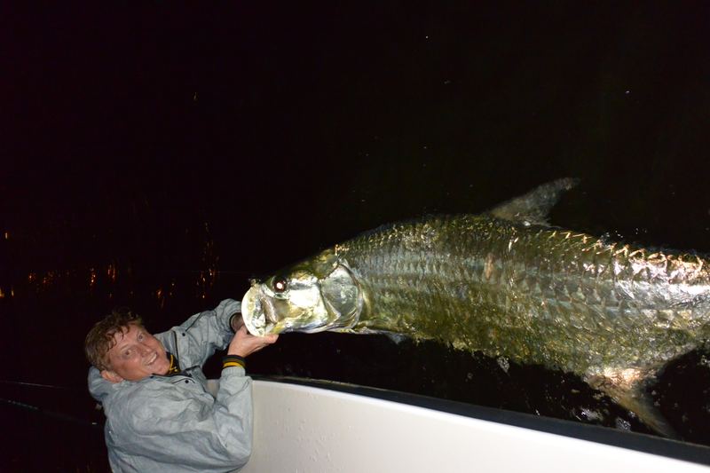 Two anglers lifting a tarpon alongside the boat at night, ready for the release