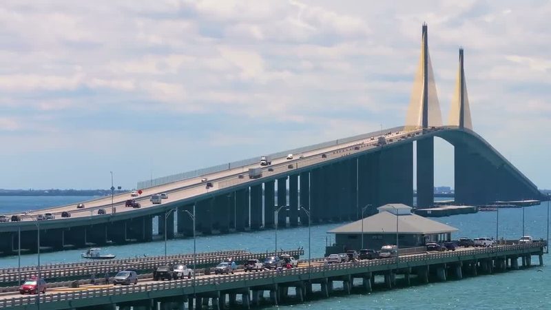 Cars and anglers parked along a fishing pier built from old bridge spans, with a cable-stayed bridge carrying traffic behind it