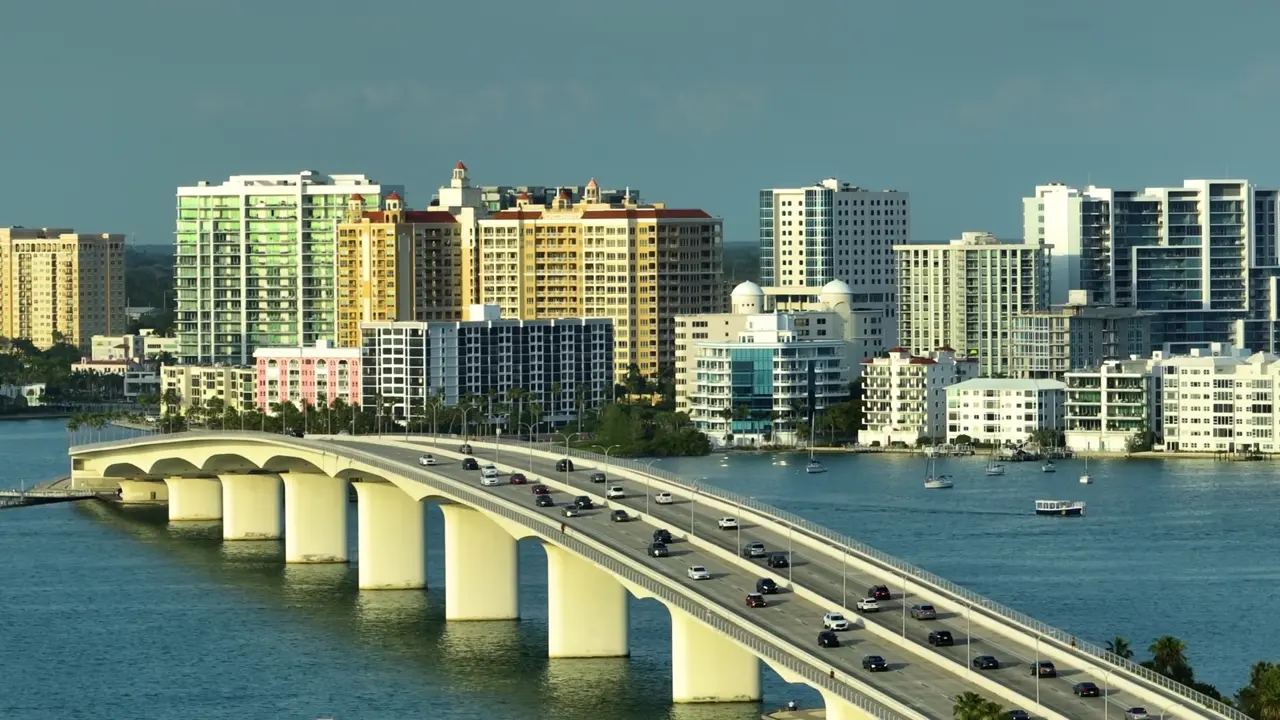 An arched causeway bridge crossing open bay water on rows of concrete piers, waterfront towers behind it