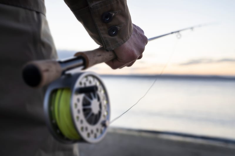 A hand holding a fly rod, floating line on the reel, flat water at first light