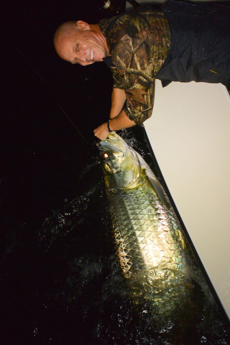 Angler in camouflage with a tarpon held boatside under spotlight