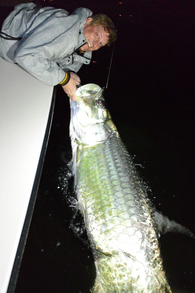 Angler in a rain jacket smiling next to a large silver tarpon at the boatside